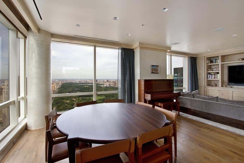 Luxurious high-rise apartment interior with panoramic city and park views, featuring modern furniture, a dining area, piano, and cozy living room with entertainment center, showcasing upscale urban living.